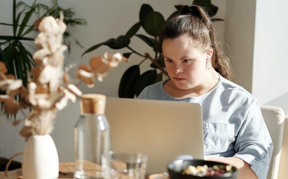 A young woman with Down syndrome works on a laptop computer.
